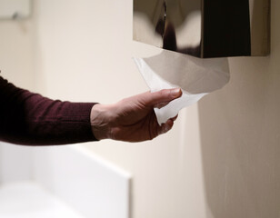 Close-up photo of a hand in a public toilet tearing off paper.