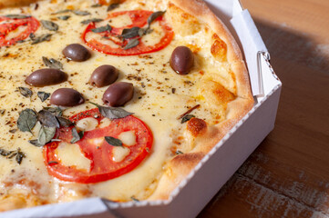 Close-up view of opened pizza box containing a "margherita" pizza on wooden table.