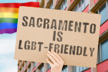 The phrase " Sacramento is LGBT-Friendly " on a banner in men's hand with blurred LGBT flag on the background. Human relationships. different. Diverse. liberty. Sexuality. Social issues. Society