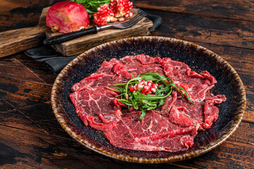 Carpaccio marbled beef meat with arugula and pomegranate seeds. Wooden background. Top view