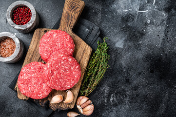 Raw veal hamburger patties with herbs and spices. Black background. Top view. Copy space