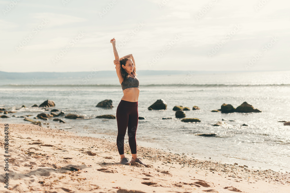 Wall mural female runner doing stretching exercise on the beach, morning run, fitness and healthy lifestyle con