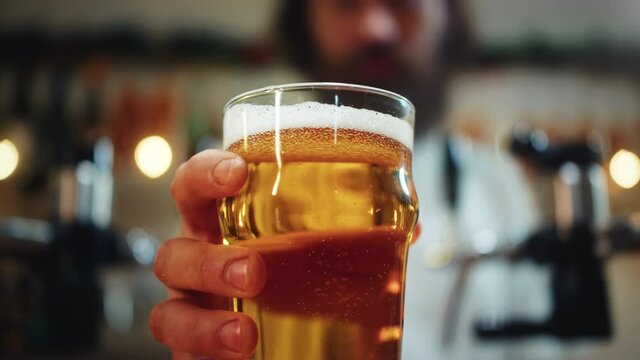 Foamy beer in glass close-up. Alcohol golden drink, barman putting beer in mug on table. Macro shooting of fresh pale ale on bar counter background in pub. 