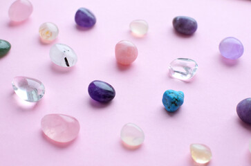 Gems of different colors. Amethyst, rose quartz, agate, apatite, aventurine, olivine, turquoise, aquamarine, rhinestone lie on a pink background. Flat lay