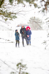 Young man in warm hat and child girl and boy on rural winter snowy background holding umbrella. Happy family, cold weather. Time together. Vacations. Snowy winter, lost in forest. Father and kids