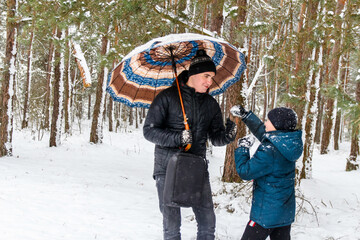 Young man and funny child boy on rural winter snowy background holding umbrella and joking. Happy family, cold weather. Lifestyle. Vacations. Snowy winter, lost in forest. Older brother. Smiling