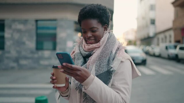 Young african american woman using smartphone and drinking coffee at street