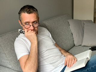Middle aged man is spending holiday at home. Looked bored of streaming tv and reading book. Self...
