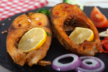 Fried carp fish slices on a black plate.  Fried golden crust fish fillets with  lemon and vegetables.