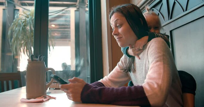 Young beautiful woman with child in restaurant watching QR code online menu choosing food for lunch. Attractive girl using smartphone waiting for her dinner in the bar. 