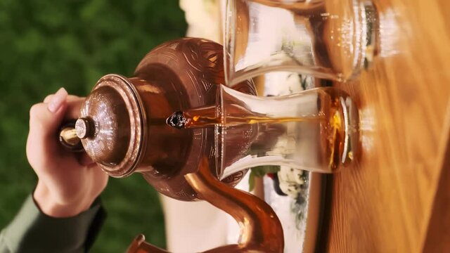 The girl pours Turkish aromatic tea into a traditional glass. Tea from two teapots is poured into a glass. Tea is poured from one teapot. Water is poured from another kettle. Close-up. Steam rises abo