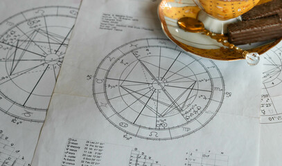 Printed astrology natal charts with yellow cup of coffee and chocolate biscuits in the background