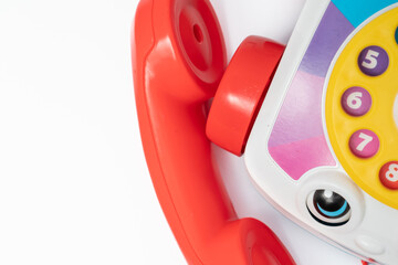 Children's toy landline phone with a red receiver, a dial and a smile on the body isolated on white