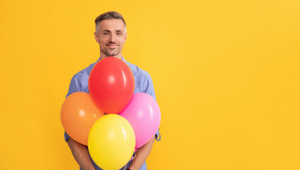 smiling handsome man hold party balloons on yellow background, copy space, shopping