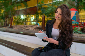 Obraz premium Young attractive business woman using a digital tablet and writing in her notebook
