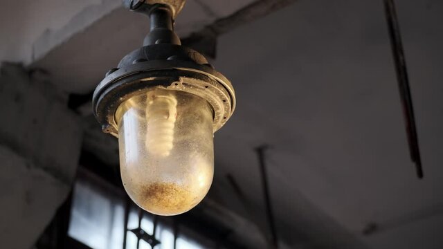 explosion-proof lamp hangs from ceiling in old abandoned factory. Non-working lamp with massive bulb. Light in darkness concept.