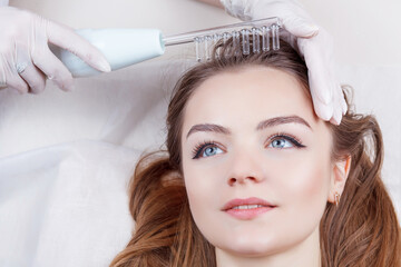 The doctor-cosmetologist makes the procedure Microcurrent therapy On the hair of a beautiful, young...