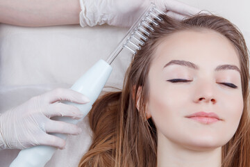 The doctor-cosmetologist makes the procedure Microcurrent therapy On the hair of a beautiful, young woman in a beauty salon.Cosmetology and professional skin care.