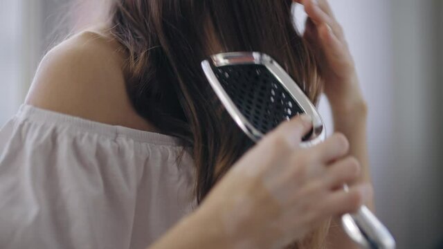 Close-up of young woman combing long curly hair, everyday beauty care rituals