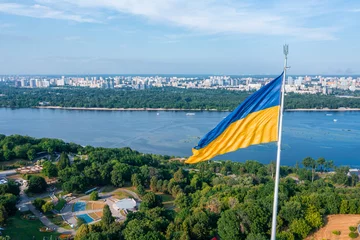 Foto op Canvas Aerial view of the Ukrainian flag waving in the wind against the city of Kyiv, Ukraine near the famous statue of Motherland. © ingusk