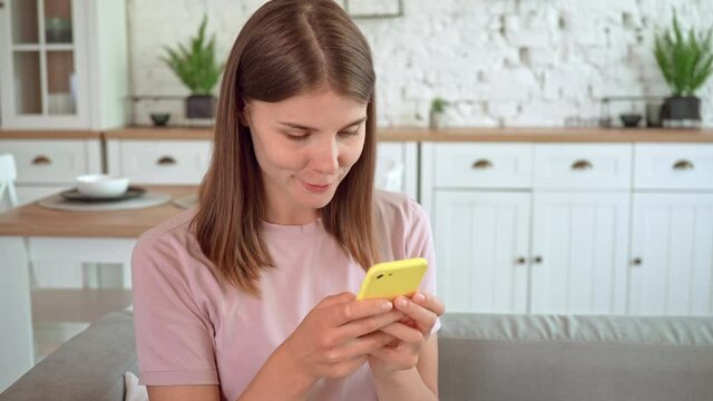 woman holding smartphone holding smartphone typing post or comments in social media sitting on the couch in living room