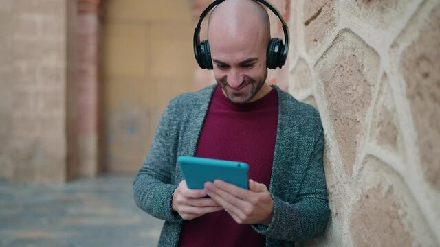 Young bald man smiling confident watching video on touchpad at street