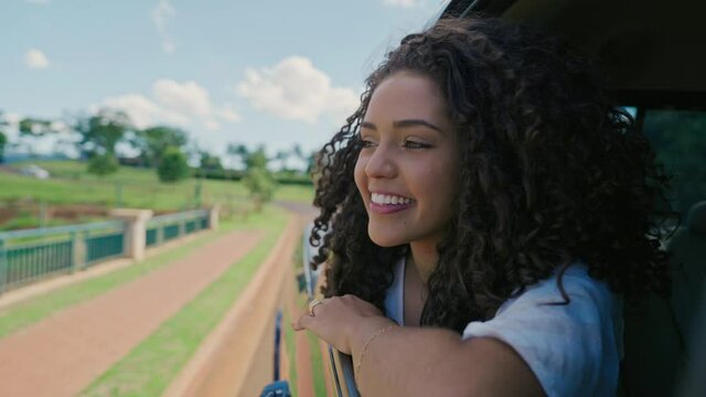 Latin woman in car window. Car trip. Curly hair in wind. Girl looks out of car window. Brazilian travel concept by car. Cinematic 4K
