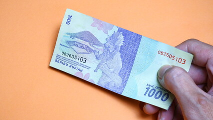 A man's hand is making a payment. Male hand showing Indonesian rupiah note. Indonesian Rupiah the...