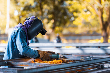 Worker using electric wheel grinding on steel structure in factory.