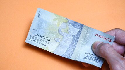 A man's hand is making a payment. Male hand showing Indonesian rupiah note. Indonesian Rupiah the official currency of Indonesia. Business and finance concept. Uang 2000 Rupiah.