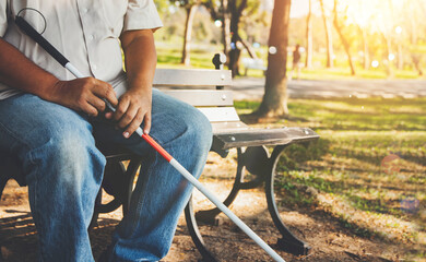 Elderly blind man with a blind cane sits alone on a park bench : Lind man who wants peace and lives...