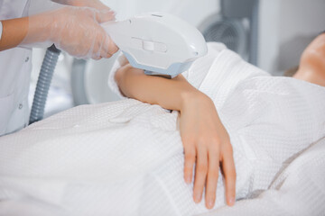 Close up laser hair removal on the arm of a young girl by a professional specialist in a modern cosmetology office