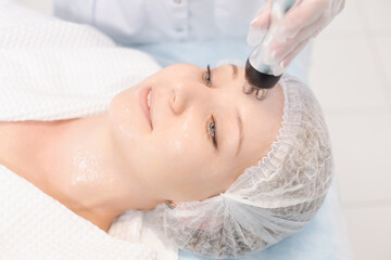 Close up portrait of a beautiful smiling woman relaxing during the RF lifting procedure in a modern beauty salon
