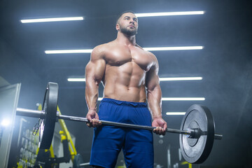 Fototapeta na wymiar Bottom up view of a muscular athlete lifting heavy barbell showing his muscles in a gym