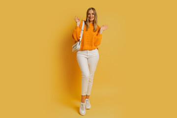 Fototapeta na wymiar Pretty blond woman in trendy autumn outfit posing on yellow background in studio. Holding white leather bag. Full lenght.