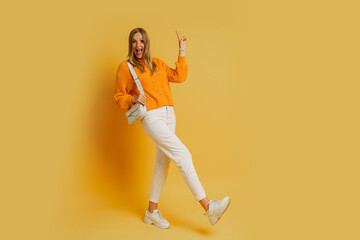 Fototapeta na wymiar Pretty blond woman in trendy autumn outfit posing on yellow background in studio. Holding white leather bag. Full lenght.