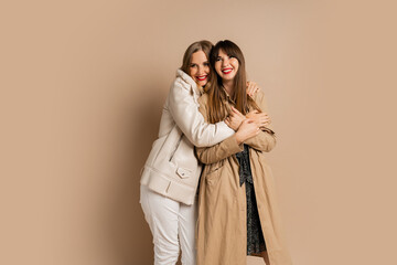 Two elegant women in stylish winter outfit posing over beige background. Wearing coat and jacket. Shopping and fashion concept.