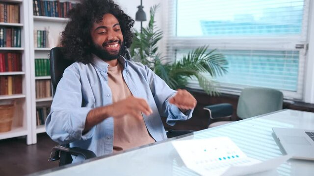 Happy young Indian man entrepreneur rejoices looking at document with financial economic indicators of business overfulfilling sales plan sits at desk in office. Businessman career success concept.
