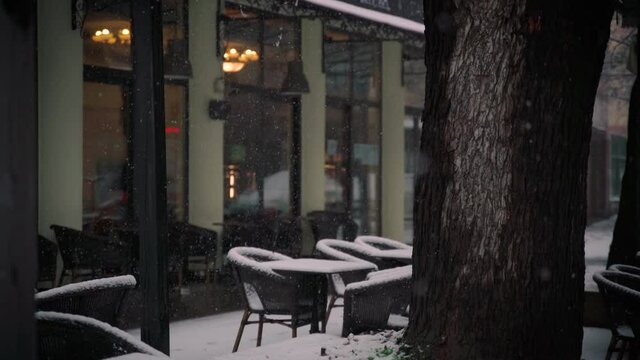 Handheld cinematic shot of a street terrace of the restaurant during snowfall, tables are covered with snow.