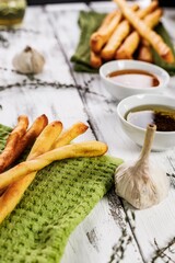 Crispy grissini breadsticks. Traditional Italian wheat bread with garlic, cheese and sesame seeds. Food still life on a white rustic background. Olive oil and green napkin. Mediterranean Food