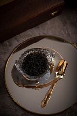 Black caviar in a crystal bowl, decorated with golden sturgeon on a dark concrete background.