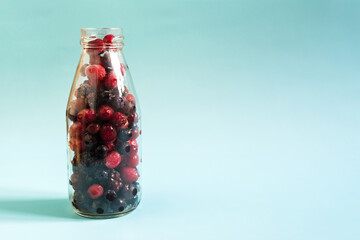 The concept of using quick-frozen berries. A mixture of frozen black and red berries in a transparent bottle on a light background
