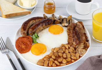 Full english breakfast with fried bacon, mushrooms, eggs, beans, sausages on a white wooden table