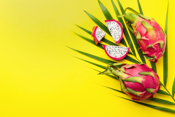 Delicious cut and whole white pitahaya fruits with palm leaf on yellow background, flat lay. Space...