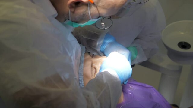 The dentist and his assistant treat the patient. Dental treatment in modern dentistry. A close-up shot of a patient in a dental chair undergoing a tooth extraction procedure. Medicine and healthcare.