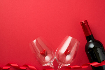 Top view photo of valentine's day decorations red curly ribbon small hearts in two wineglasses and wine bottle on isolated red background with empty space