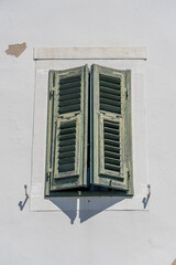 Window with green wooden shutters on old white stucco wall and copy space