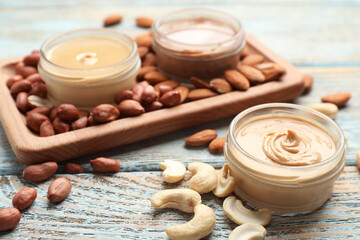 Different types of delicious nut butters and ingredients on light blue wooden table, closeup