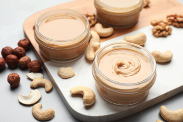 Different types of delicious nut butters and ingredients on light table, closeup