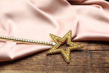 Fototapeta na wymiar Beautiful golden magic wand and pink fabric on wooden table, closeup